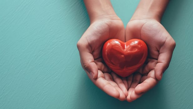 Hands holding a red heart on a green background. The concept of love and health.