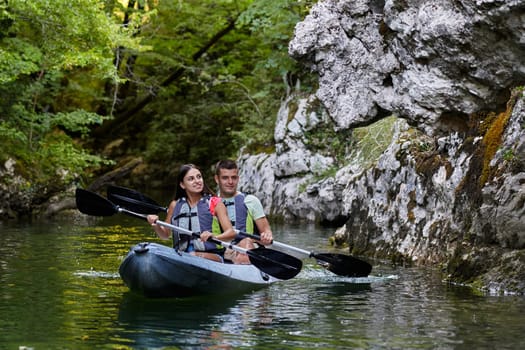 A young couple enjoying an idyllic kayak ride in the middle of a beautiful river surrounded by forest greenery.