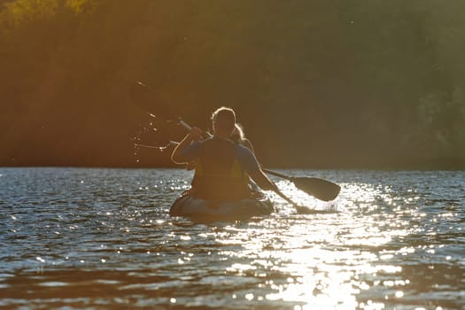 A young couple enjoying an idyllic kayak ride in the middle of a beautiful river surrounded by forest greenery in sunset time.