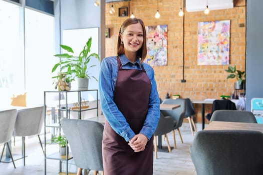 Attractive successful young woman service worker, business owner in apron looking at camera in restaurant cafeteria coffee pastry shop interior. Small business staff occupation entrepreneur work