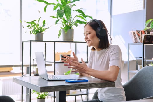 Young woman in headphones having work video chat conference call using laptop computer sitting in cafe coworking. Remote virtual online work study freelance blog vlog, internet technology youth concept