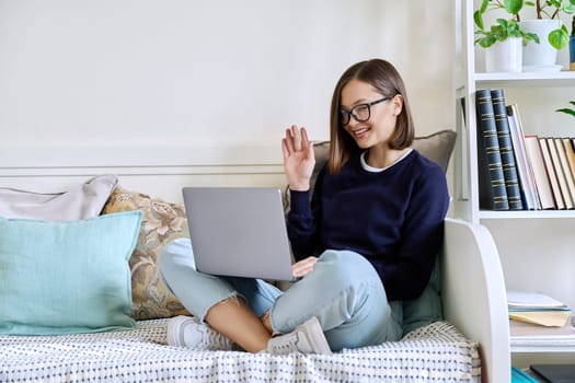 Young woman sitting with laptop on couch at home having video call. Female chatting with friends colleagues on social networks student talking in online lesson freelancer working remotely on computer