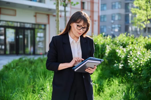 Portrait of business mature confident successful woman with digital tablet outdoor, educational office building background. Office employee school teacher insurance banking law firm real estate agent