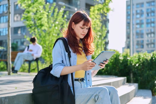 Young attractive female college student using digital tablet outdoor, educational building background. Education, technology, training, 19,20 years age youth concept