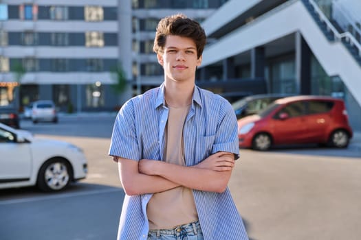 Portrait of confident smiling college student guy, young handsome male with crossed arms looking at camera, urban city outdoor. Education, lifestyle, 19,20 years age youth concept