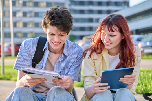 Teenage college students guy and girl talking, using digital tablet, sitting outdoor, urban modern city. Youth 19-20 years old, education, technologies, lifestyle, friendship concept