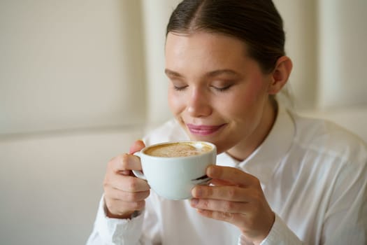 Close-up of an elegant beauty adult caucasian woman smelling a delicious coffee in a modern cafeteria