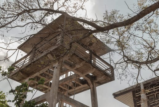 Bottom up view of Branches of tree in front of Old water tower made of Cement and metal staircase with sky background. Selective focus. Selective focus.