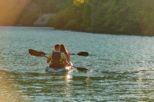 A young couple enjoying an idyllic kayak ride in the middle of a beautiful river surrounded by forest greenery in sunset time.