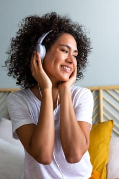 Happy young African American latina woman listening to music using headphones at home bedroom. Lifestyle concept.