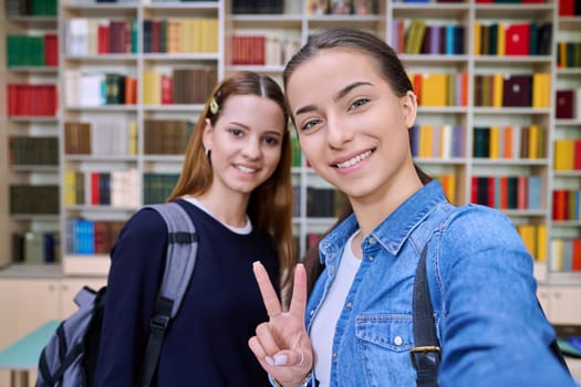 Selfie portrait of happy friends teenagers high school students looking at camera inside classroom. Smiling cheerful two teenage girls in library. Friendship adolescence education lifestyle concept