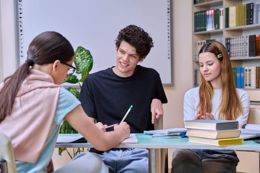 Group of high school students are studying in library class, classmates are laughing talking discussing together, team study project, preparing for tests and exams. Education adolescence communication