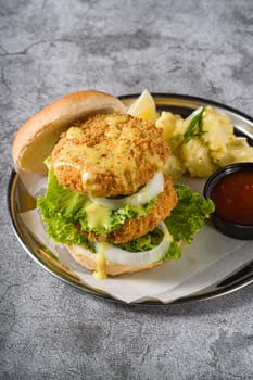 Double fish burger with potato salad on a metal plate