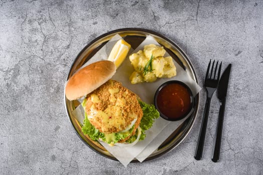 Double fish burger with potato salad on a metal plate