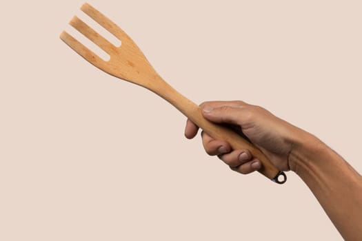 Hand holding wooden fork on beige background cutout. High quality photo