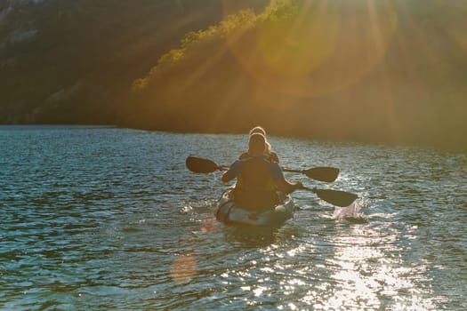 A young couple enjoying an idyllic kayak ride in the middle of a beautiful river surrounded by forest greenery in sunset time.