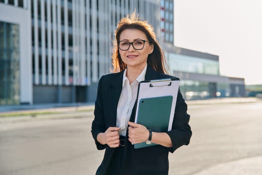 Outdoor portrait of middle aged business woman agent manager holding digital tablet clipboard, on street of modern city. Business marketing work financial services rental real estate sales insurance