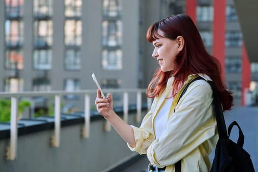 Young female using smartphone, modern city background. Teenage student 19-20 years old, texting using mobile apps applications for leisure study travel. Technology Internet education youth urban style
