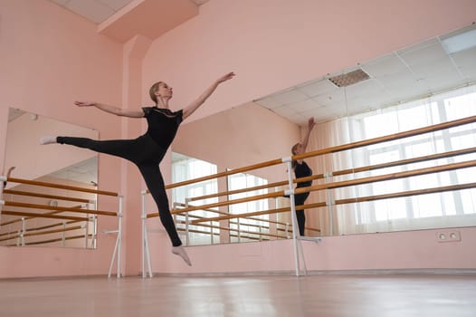 Caucasian blonde woman is practicing ballet in class. Ballerina rehearsing at the barre