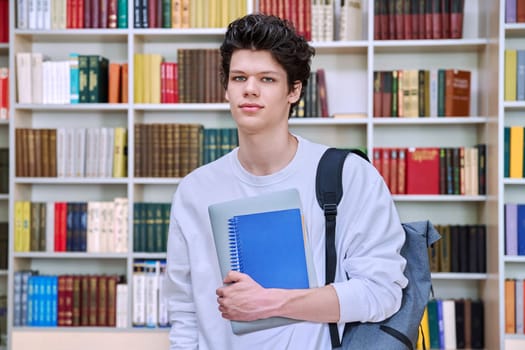 Portrait of confident handsome college student teenage male 19, 20 years old inside library of educational building. Education, youth, lifestyle concept