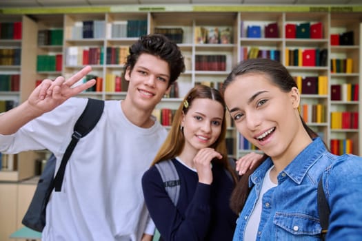 Selfie portrait of group friends teenagers high school students looking at camera inside classroom. Having fun cheerful teenage guy and two girls in library. Friendship adolescence education lifestyle