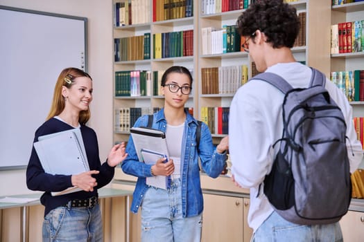 Group of teenage high school students in library classroom. Three schoolchildren 16, 17 years old, talking laughing together. Education, adolescence, friendship communication concept