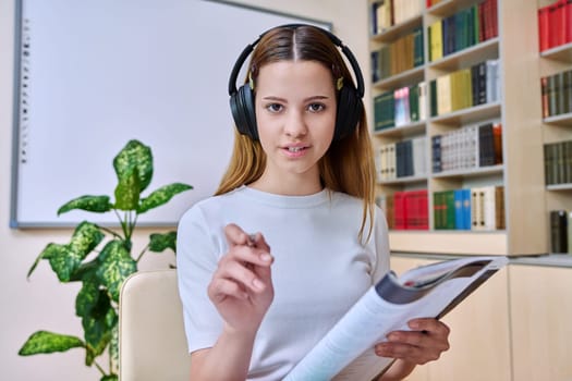 Webcam view of teenage girl, high school student, in headphones, talking to camera. Female teenager studying remotely, video conference chat, online test exam lesson. Technology education adolescence