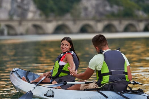 A young couple enjoying an idyllic kayak ride in the middle of a beautiful river surrounded by forest greenery.