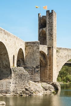 The medieval bridge of Besalú, Girona, with one of its towers with two flags on top. The bridge is over the Fluvià river. 