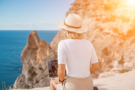 Freelance women sea working on the computer. Good looking middle aged woman typing on a laptop keyboard outdoors with a beautiful sea view. The concept of remote work