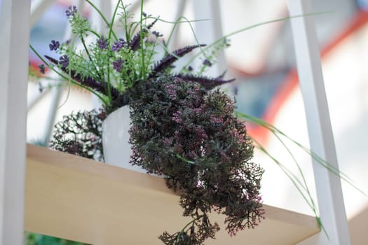 A beautiful white vase holding vibrant purple flowers is placed on a sturdy wooden shelf, creating a lovely display of nature and artistry