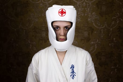 Young woman in kimono and protective helmet for kyokushinkai karate with a serious face looking at the camera. Inscription in Japanese: Kyokushinkai