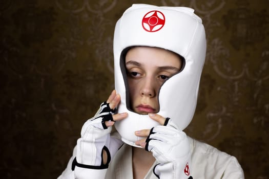 Girl in kimono and special Kyokushin karate gloves puts on protective helmet before fight, safety of martial arts athletes