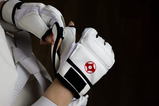 Female hands put on special Kyokushin karate fighting gloves for fight in Japanese martial arts. White karate gloves with red Kyokushinkai symbol on the athlete to protect his hands