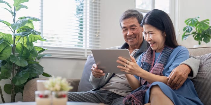 Senior couple happily using tablet at home. Concept of technology, companionship, and relaxation.