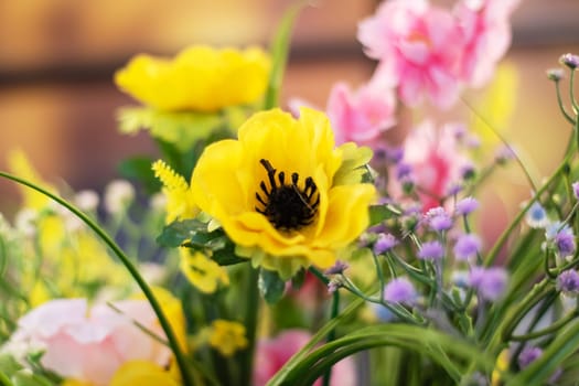 In a field, a bright yellow flower with a dark center stands out, amidst a cluster of other vibrant flowers in full bloom