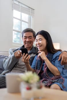 Senior couple smiling while using smartphone at home. Concept of technology, companionship, and relaxation.