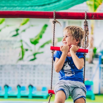 Smiling child preschool boy on rope ladder. Bright emotions. Happy childhood, enjoy life be yourself.