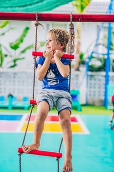 Smiling child preschool boy on rope ladder. Bright emotions. Happy childhood, enjoy life be yourself.