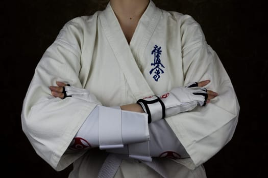 Girl in kimono and protective equipment for Kyokushinkai karate crossed her arms on her stomach, equipped fighter for martial arts. Inscription in Japanese: Kyokushinkai