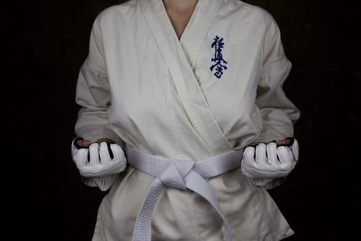Girl athlete in kimono and white belt in Kyokushin karate stands in stance with clenched fists with reverse grip, concept of karate athlete. Inscription in Japanese: Kyokushinkai
