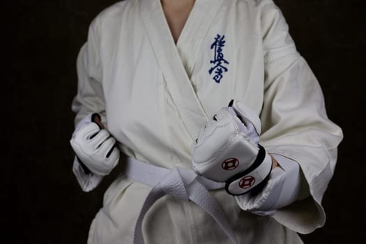 Young woman in Kyokushin karate kimono in fighting stance with lowered clenched fists in special protective gloves in front of her opponent. Inscription in Japanese: Kyokushinkai