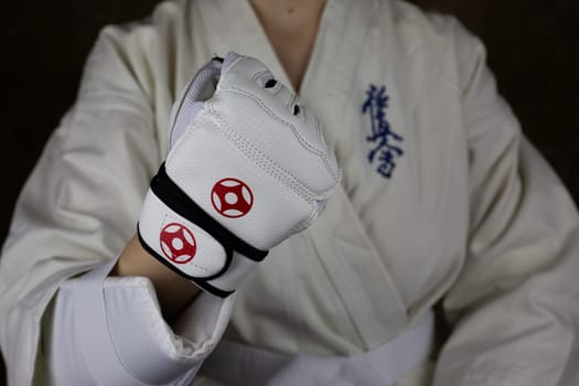 Girl athlete in Kyokushinkai karate demonstrates clenched fist in special protective glove for martial arts. Athlete in karate kimono. Inscription in Japanese: Kyokushinkai