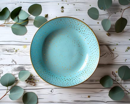 A rectangular aqua plate with gold polka dots sits on a wooden table adorned with eucalyptus leaves, serving as beautiful tableware surrounded by natural greenery