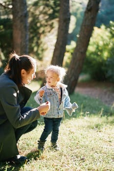 Little girl looks at her mother crouching next to her in the forest. High quality photo