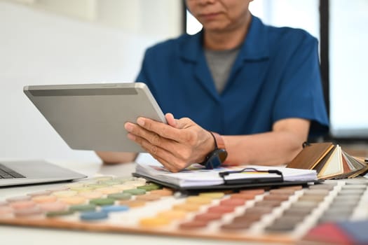 Senior male decorator or interior designer drawing a sketch on a digital tablet at desk.