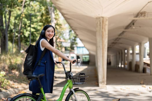 Businesswoman commuting by bicycle with headphones in urban park. Concept of eco friendly transport, active lifestyle, and outdoor fitness.