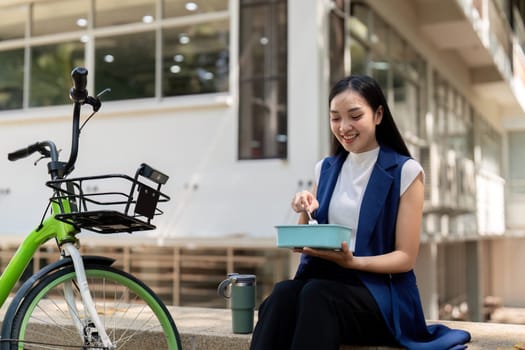 Businesswoman enjoying a lunch break outdoors with her bicycle parked nearby. Concept of work life balance, healthy eating, and sustainable commuting.