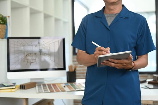 Cropped shot of senior male interior designer holding digital tablet in a modern creative studio.