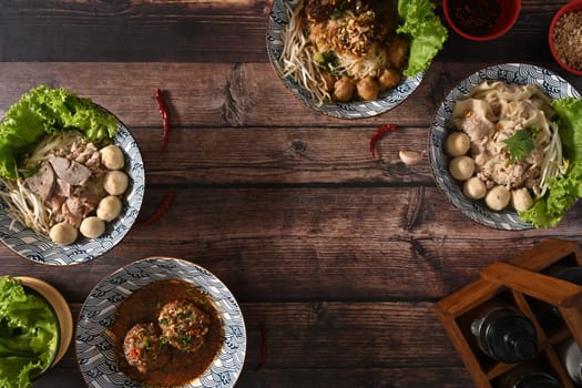 Tasty spicy Thai noodles, scalded meatball and condiment set for seasoning on wooden table.
